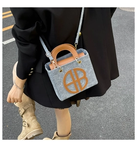 Close-up of grey felt tote bag featuring a leather AB logo and brown top handles