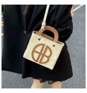 Close-up of stylish contrast tote bag with large leather AB logo on office lady outfit