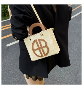 Detail of a minimalist square crossbody bag in cream and brown leather on a model