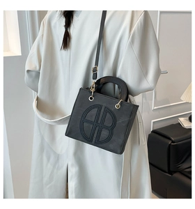 Detail of minimalist black crossbody bag with embossed AB logo on beige wool coat