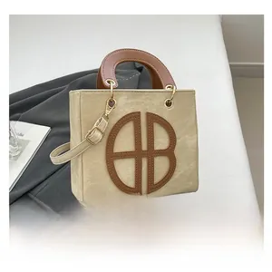 Close-up of beige canvas tote with brown leather handles and circular AB leather logo
