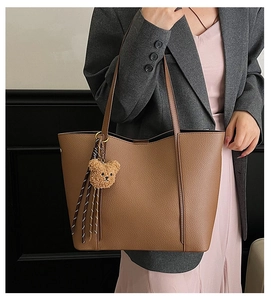 Brown lychee leather tote bag featuring a cute plush bear charm and woven tassel detail