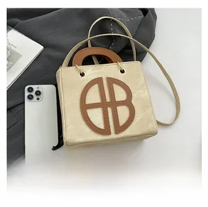Detail view of cream tote bag with large AB letter appliqué and brown top handle