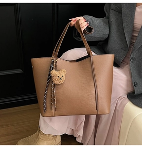 Detail of brown litchi pattern leather tote bag with cute bear charm and striped cord
