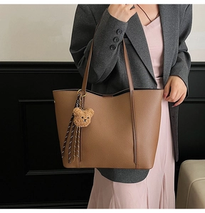 Detailed texture of brown lychee grain leather tote bag with cute bear charm and tassel