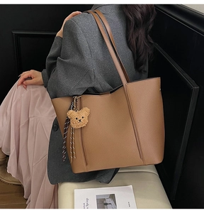 Detail of brown leather tote bag with lychee grain texture and cute bear charm