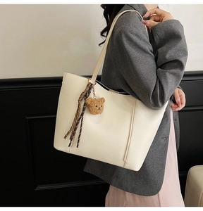 Detail of off-white lychee textured tote bag with cute bear charm and striped ribbon