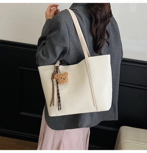 Detail of minimalist cream tote bag with litchi texture and cute bear pendant charm