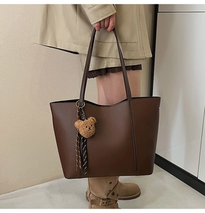 Detail of dark brown pebble leather tote bag featuring a cute bear plush keychain charm