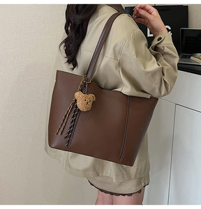 Detail view of brown lychee leather tote bag with teddy bear charm and tassel on the side