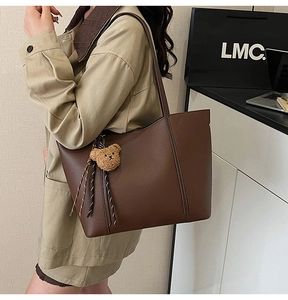 Detail of brown textured tote bag with cute plush bear charm and side tassel accents