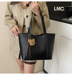 Detailed texture of black leather tote bag featuring a plush bear and striped ribbon