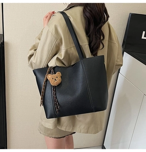 Detail of black pebbled leather tote bag with a cute bear charm on a model