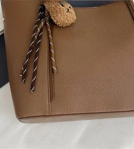 Detail of brown tote bag showing litchi texture, woven rope and plush bear pendant