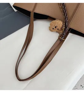 Detail of brown litchi pattern tote bag with long shoulder strap and bear charm