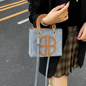Gray fabric tote bag with brown leather accents and round B patch in urban street style