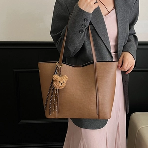 Brown large capacity leather tote bag with bear charm shown on a stylish female model