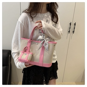Detail of canvas tote bag featuring pink trim, mini charm pouch, and decorative grey bow scarf