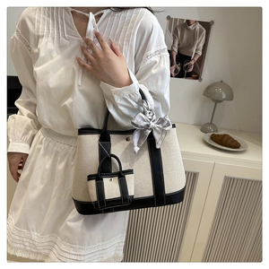 Detail of beige canvas tote with black leather trim, mini charm, and silk scarf accent