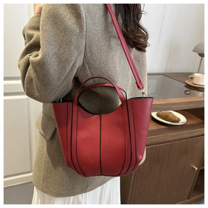 Detail showing red leather handbag with black contrast trim on a model in a warm room