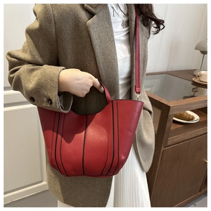 Detail of red vegan leather tote bag with black stripes styled with elegant suit and skirt