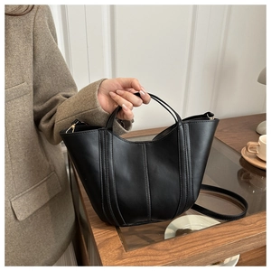 Detail of black matte bucket bag with stitching held in a minimalist cafe setting
