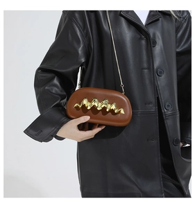 Detail der braunen Kapseltasche mit goldenem Wellendekor und schlanker Kette