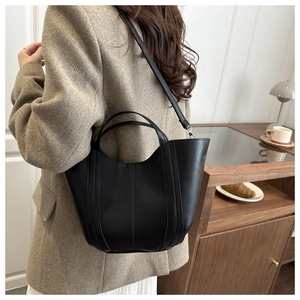 Detail of a black leather bucket bag with vertical stitching shown in a modern interior