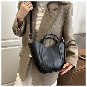 Detail of a black leather bucket bag with vertical stitching and adjustable shoulder strap