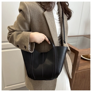 Detail of black matte leather bucket bag with vertical stitching shown on model shoulder