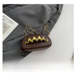 Detailansicht der dunkelbraunen Abendtasche mit goldener Wellenstruktur am Metallgriff