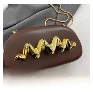 Nahaufnahme der dunkelbraunen Abendtasche mit goldener Wellenverzierung und Kettenriemen