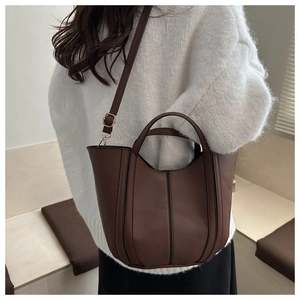 Brown PU leather bucket bag with vertical stitching shown on model with white sweater