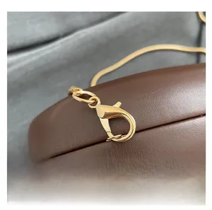 Makrodetail eines hochwertigen goldenen Metallkarabiners an einer Wellenmuster-Abendtasche