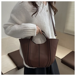 Detail of dark brown bucket bag showing vertical stitching and gold hardware