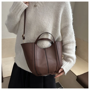 Detailed view of a brown faux leather bucket bag with black vertical stitching and top handles