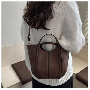 Side view of dark brown leather bucket bag on model wearing white knit sweater