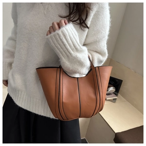 Detail shot of brown bucket bag featuring black vertical stitching and leather handle