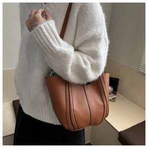 Detailed side view of caramel bucket bag with black piping on a knit sweater