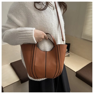 Brown bucket bag detail showing contrast stripes and detachable shoulder strap on model