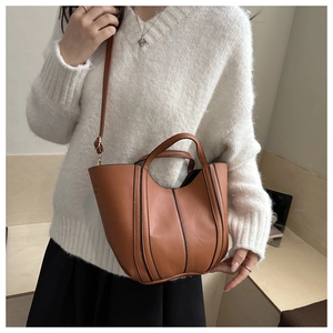 Brown leather bucket bag with vertical stripe details worn with a white sweater
