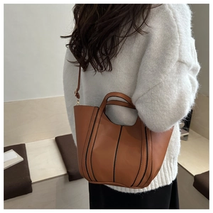 Detail of a brown bucket bag with black vertical stripes and adjustable shoulder strap