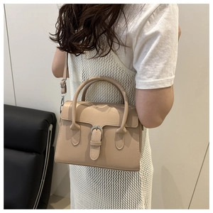 Close-up of minimalist beige crossbody bag featuring leather strap buckle and top handle