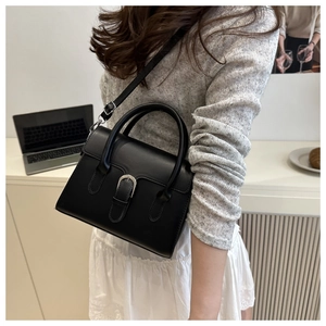 Close-up of structured black minimalist handbag showing smooth faux leather and retro clasp