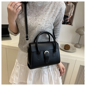 Detailed close-up of a black leather handbag with a silver horseshoe buckle and shoulder strap