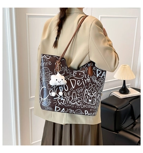 Detail of large brown graffiti tote bag with plush cloud charm shown on model's shoulder