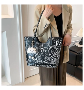 Detail of black tote bag with white graffiti patterns and cloud plush charm on a model