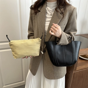 Minimalist black leather bucket bag and canvas tote shown by model in minimalist style