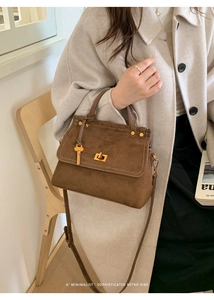 Detail of a brown suede handbag with golden twist lock and a key pendant accessory