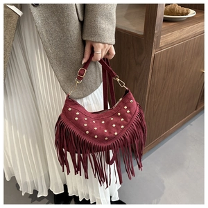 Close-up of burgundy suede crescent bag featuring golden studs and long fringe details